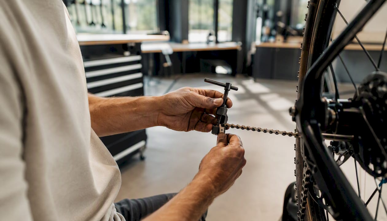Een man is bezig met het verwijderen van een schakel uit zijn fietsketting met een kettingpons.