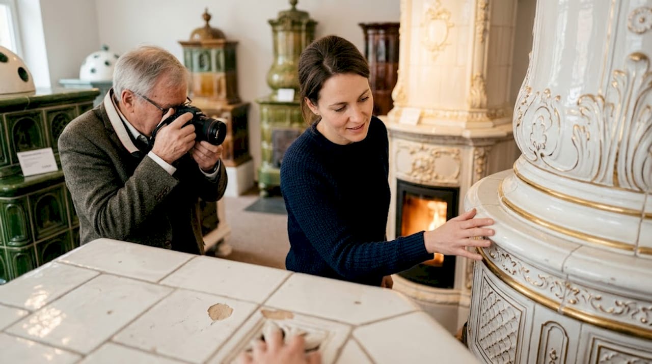 Eine Frau streicht im Ausstellungsraum über einen Rokoko-Kachelofen.