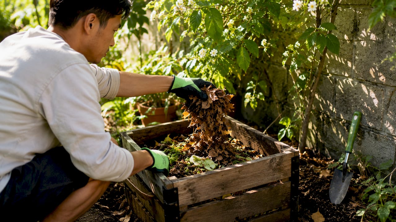 Gloved hand layering Browns in compost bin