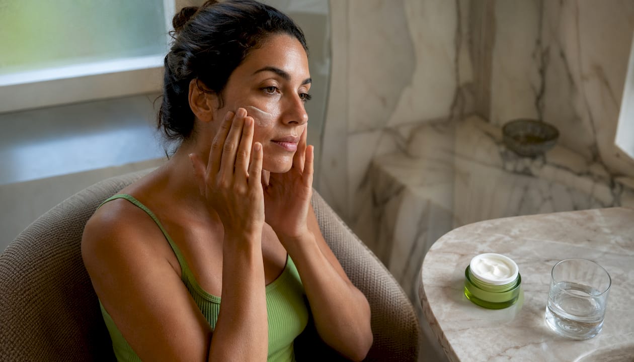 Woman applying moisturizer sitting by window