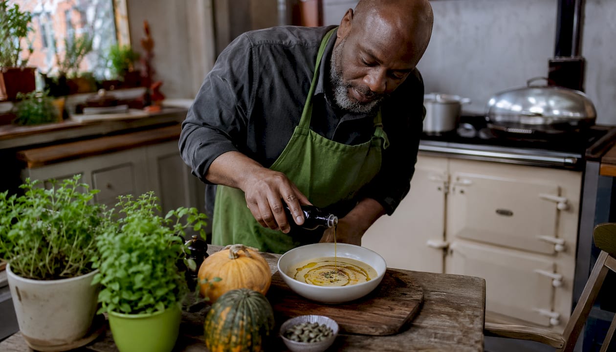 Man drizzling cold pressed oil in kitchen