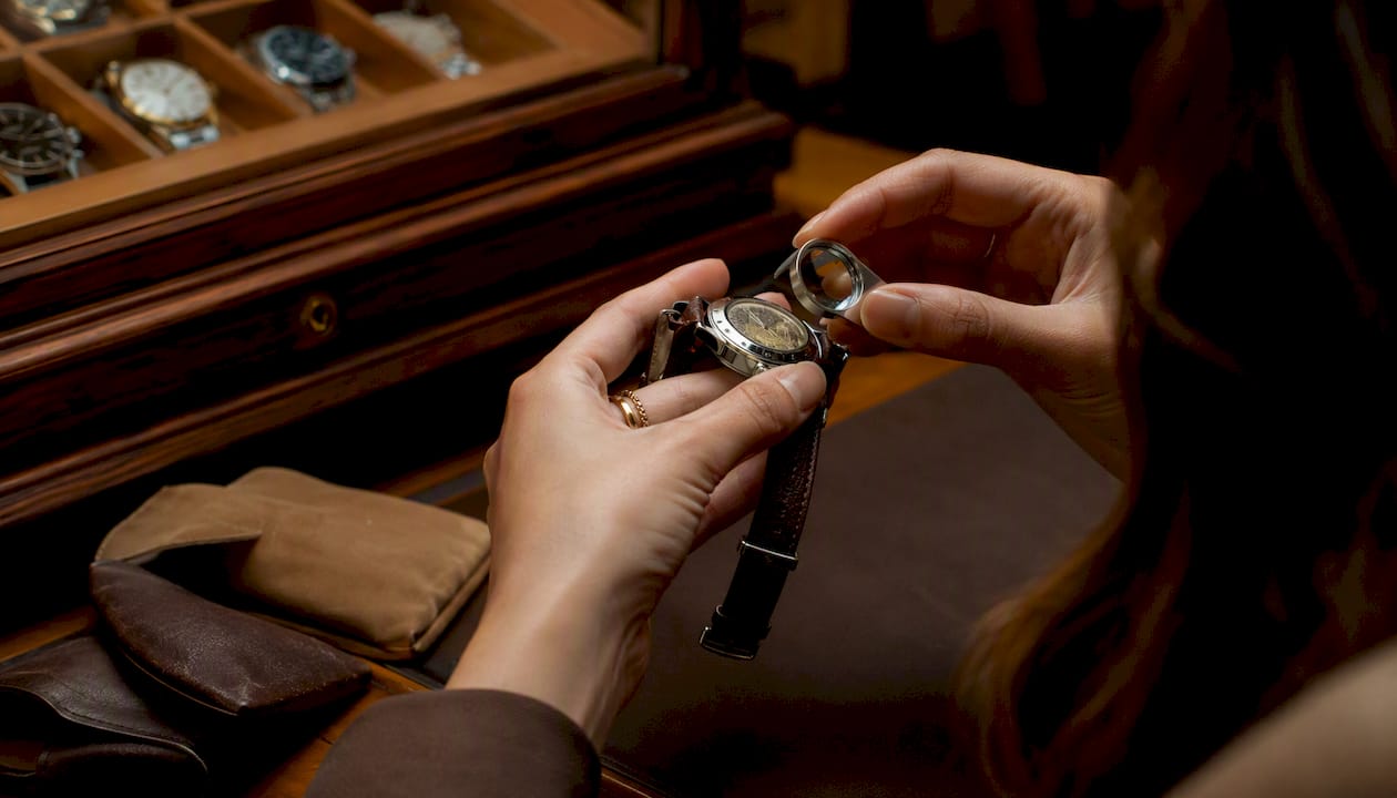 Hands inspecting Rolex with loupe at jeweler bench