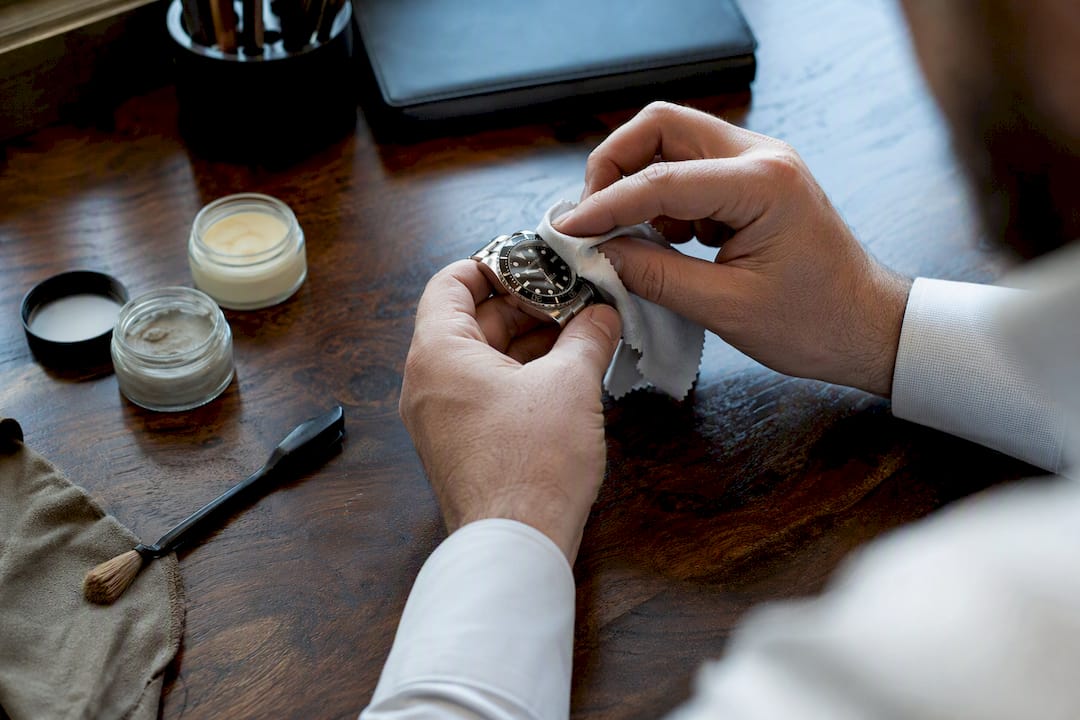 Hands polishing luxury watch bezel on wooden desk