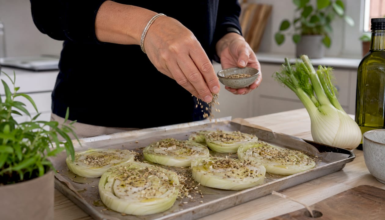 On assaisonne des tranches de fenouil disposées sur une plaque de cuisson.