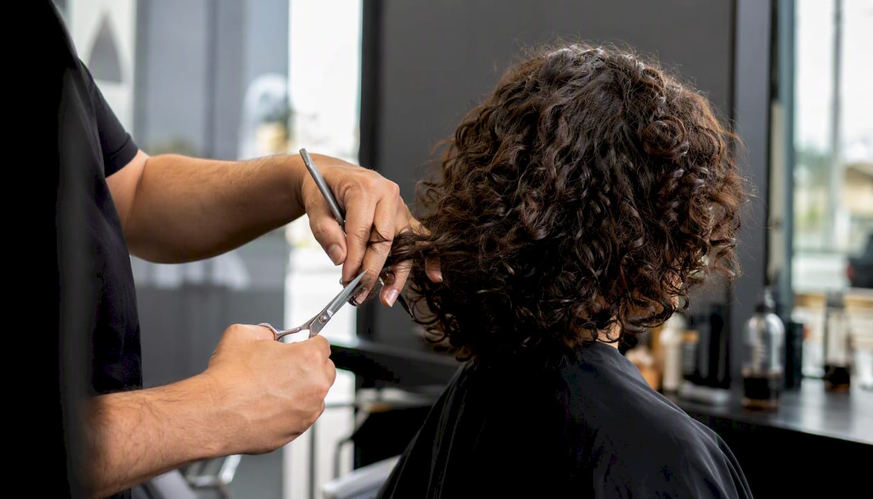 Cabeleireiro a cortar camadas de cabelo encaracolado abaixo da linha do maxilar