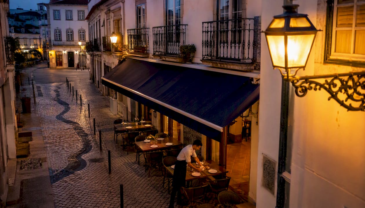 Rua típica do centro histórico, com um café acolhedor e luz ambiente a criar um cenário convidativo.
