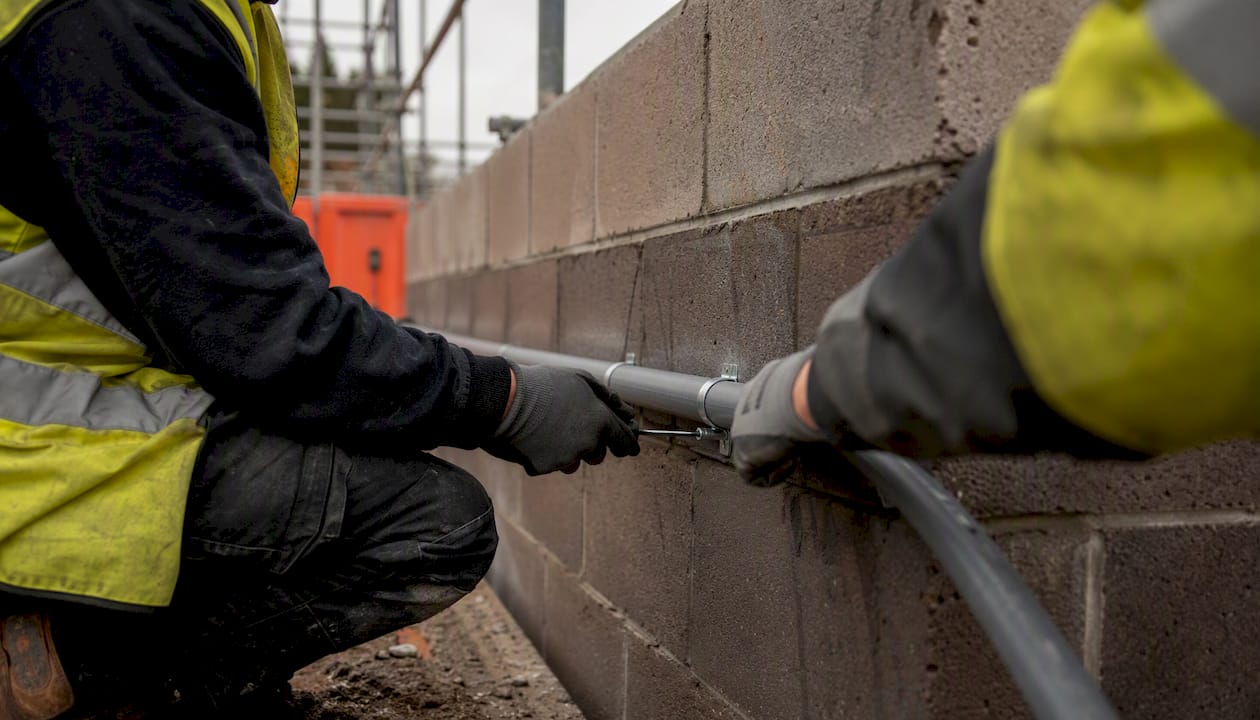 Tradespeople fitting conduit on construction wall