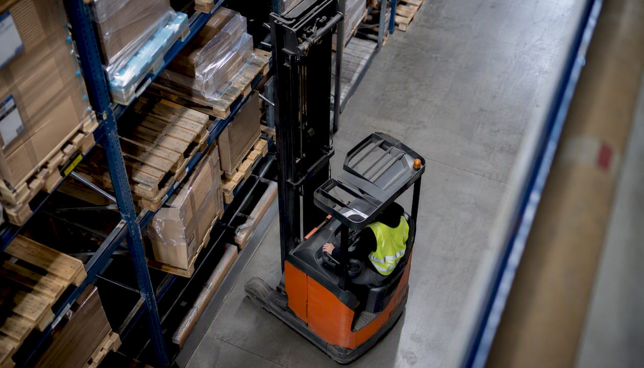 Een reachtruckchauffeur is bezig met het verplaatsen van goederen in het magazijn.