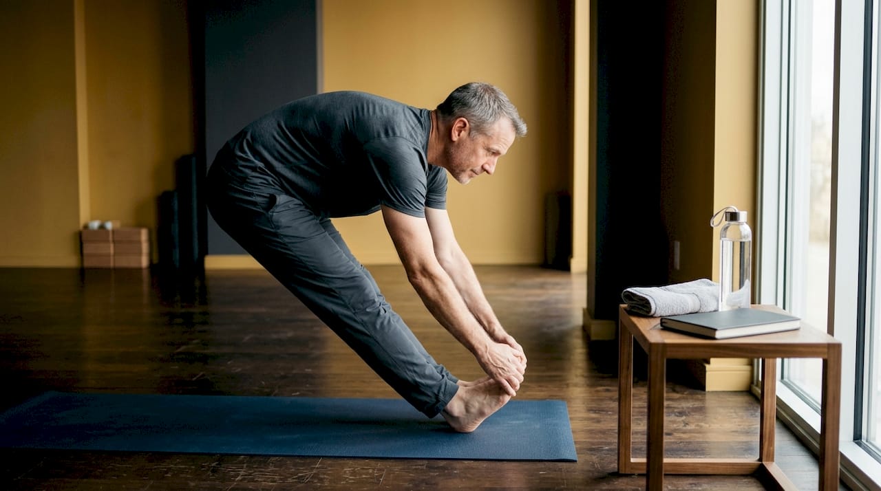 Dimineața, un bărbat își începe ziua făcând exerciții de întindere pe covorașul de yoga.