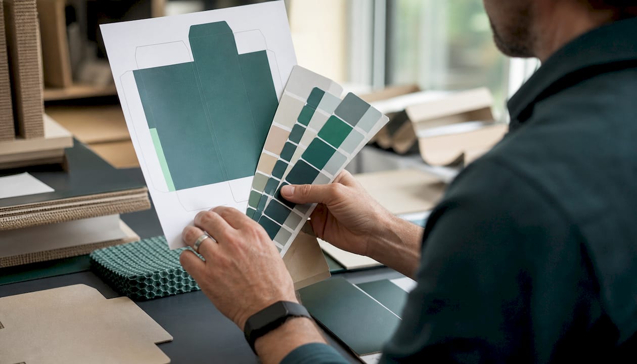 Hands comparing packaging proof and Pantone colors
