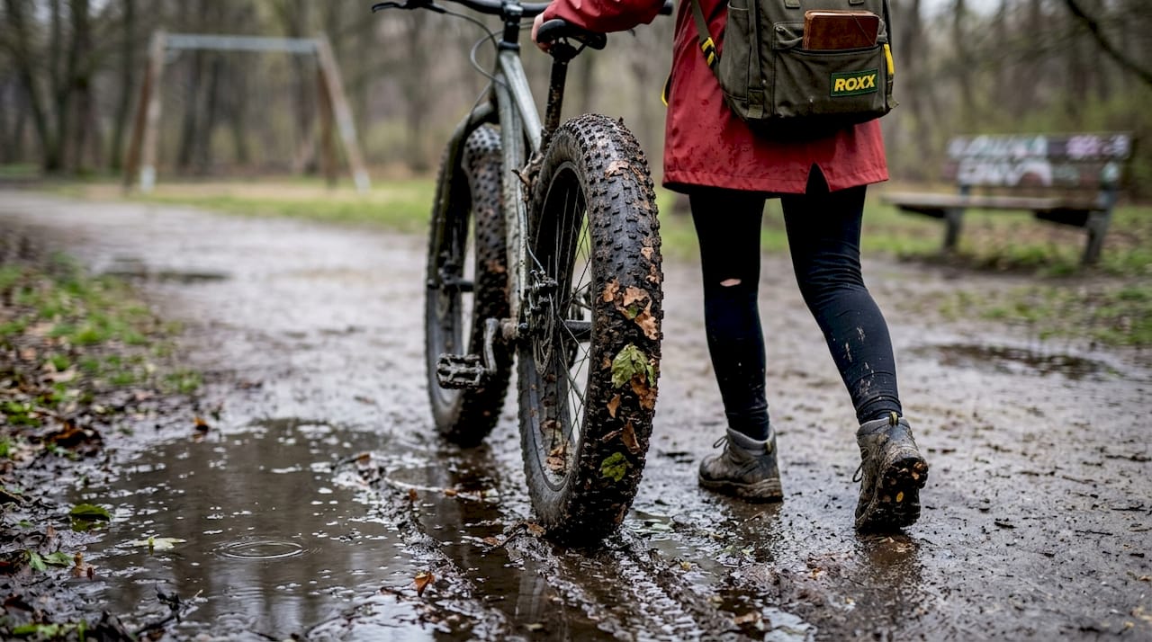Een puber rijdt met zijn fatbike over een natte parkweg.