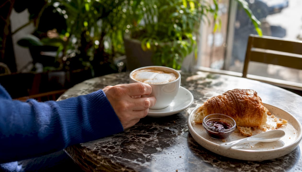 Een hand grijpt naar een kop koffie in een rustige koffietent.