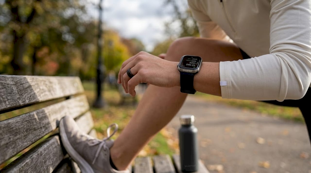 Woman checks smartwatch and wears connected ring outside