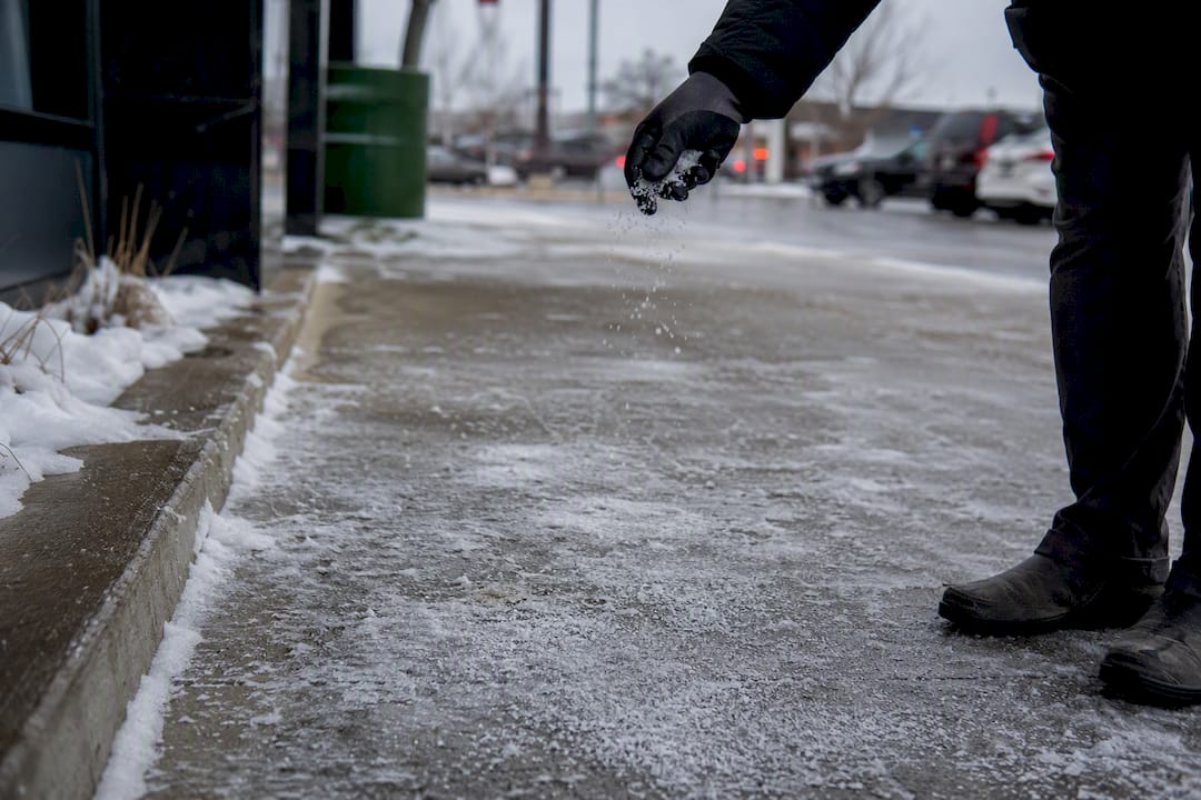 Gloved hand spreading salt on icy sidewalk