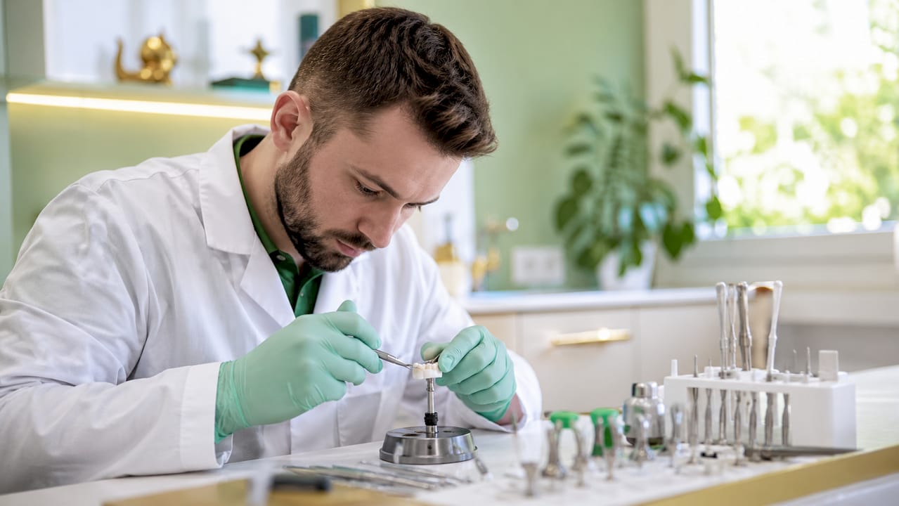 Mâini de tehnician montând o lucrare protetică fixă pe implanturi dentare