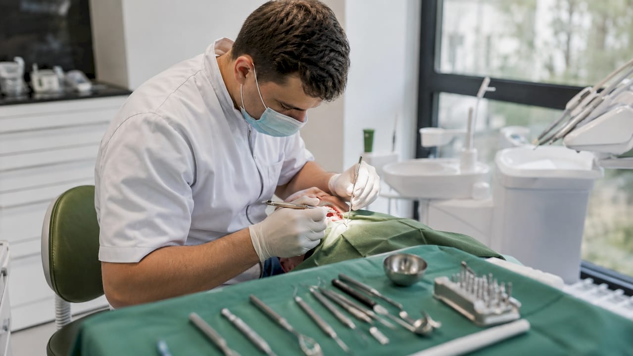 Mâinile medicului stomatolog în timpul procedurii de inserare a implantului dentar