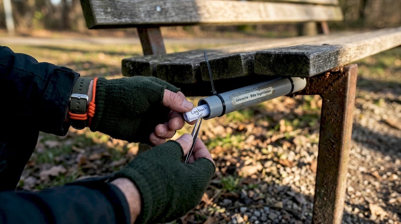 Eine Geocaching-Dose, die clever als Rohr getarnt unter einer Parkbank versteckt ist.