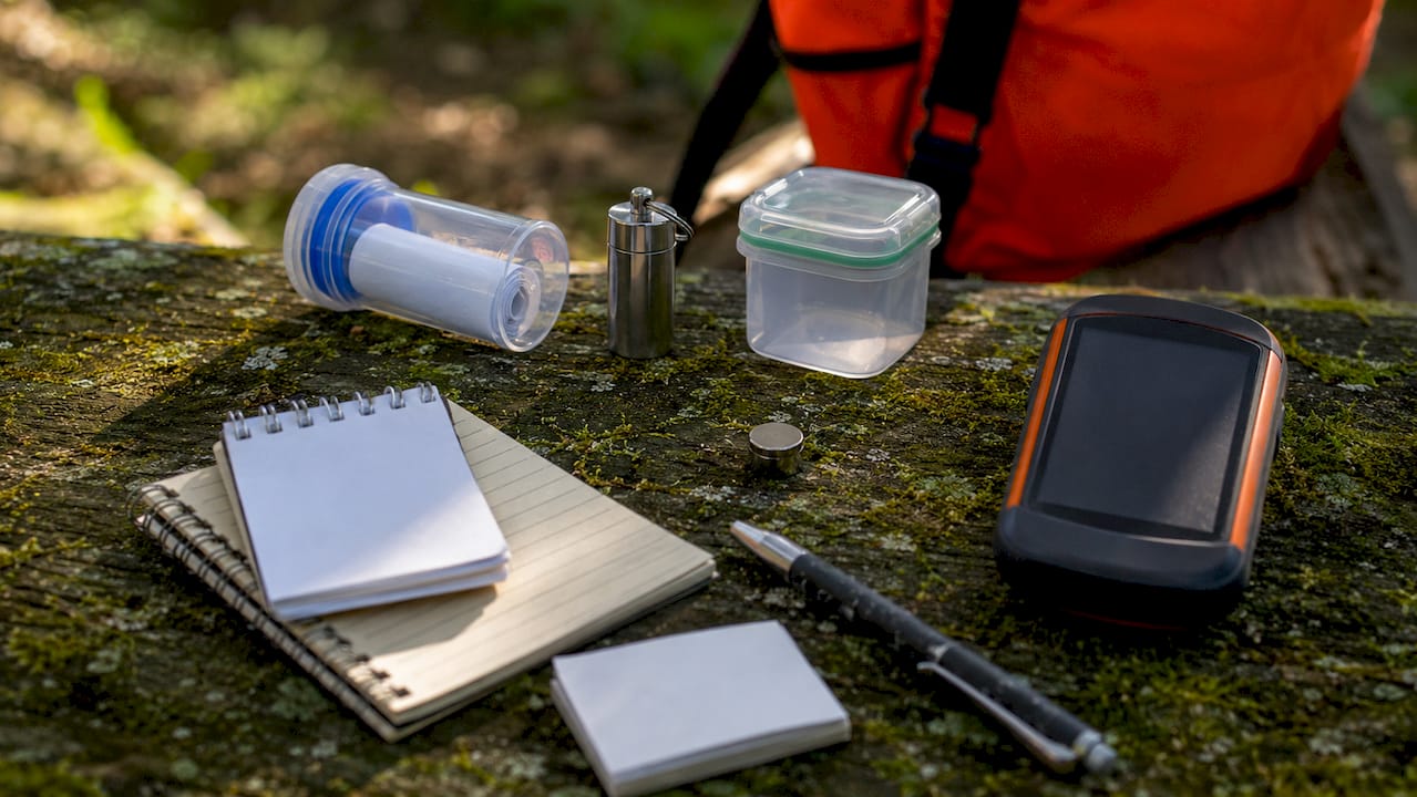 Auf dem Tisch liegen verschiedene Geocache-Dosen, die sich in Form und Größe unterscheiden.