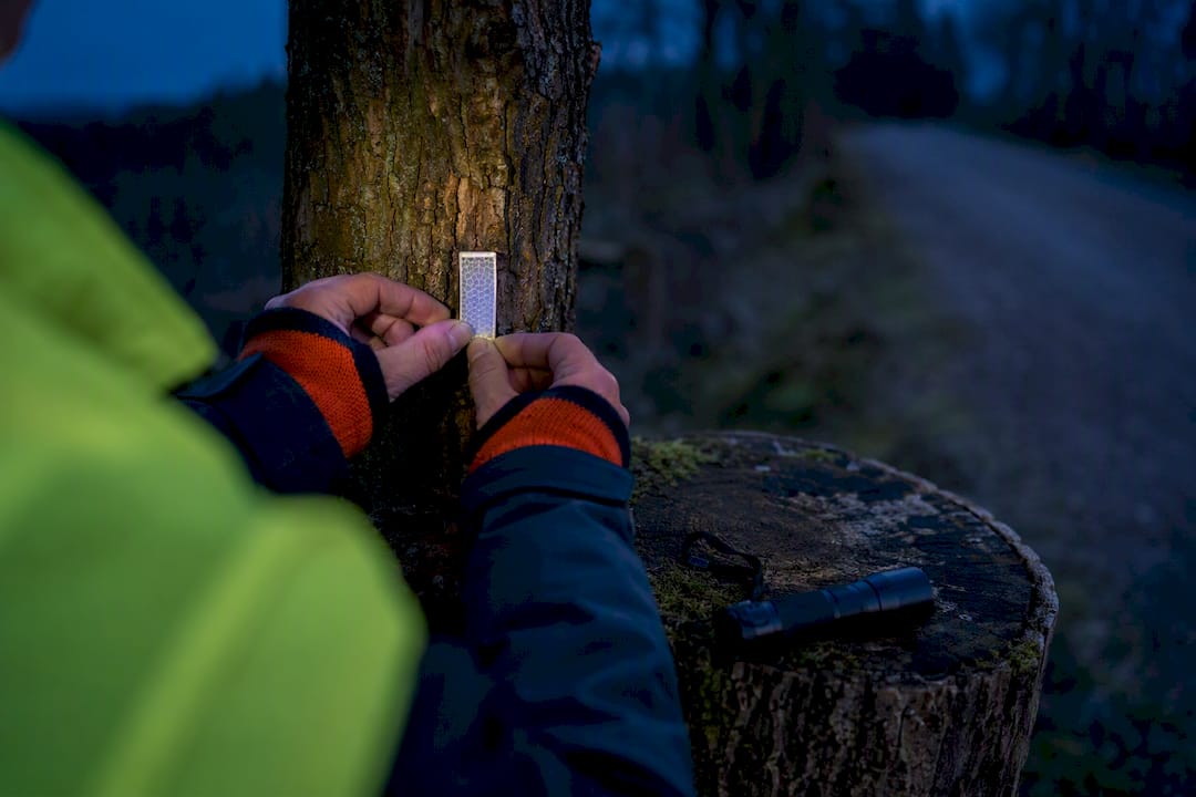 Person mit Warnweste kontrolliert Reflektor am Waldweg