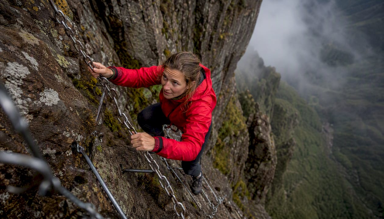 Hands gripping steel chain ladder on basalt cliff