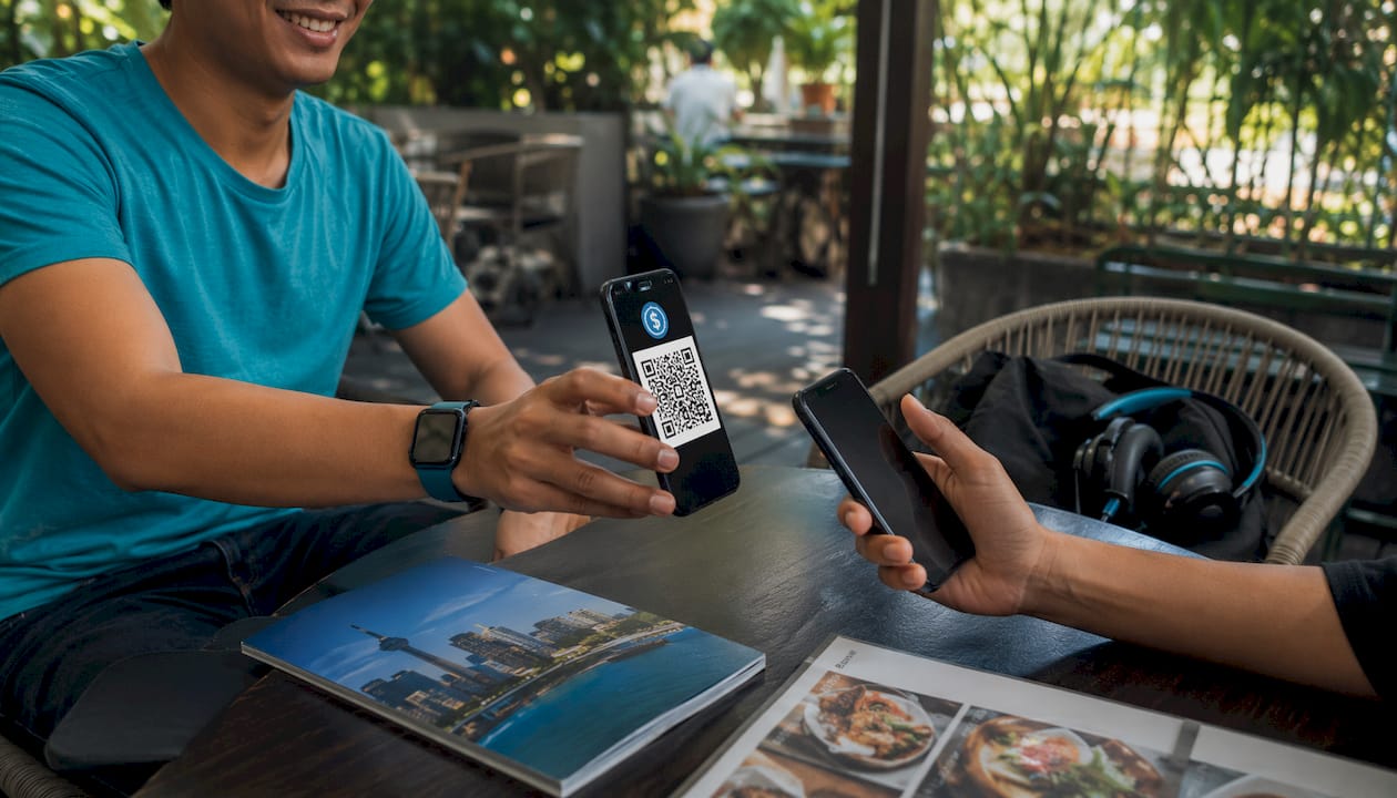 Hands exchanging crypto wallet QR code at table