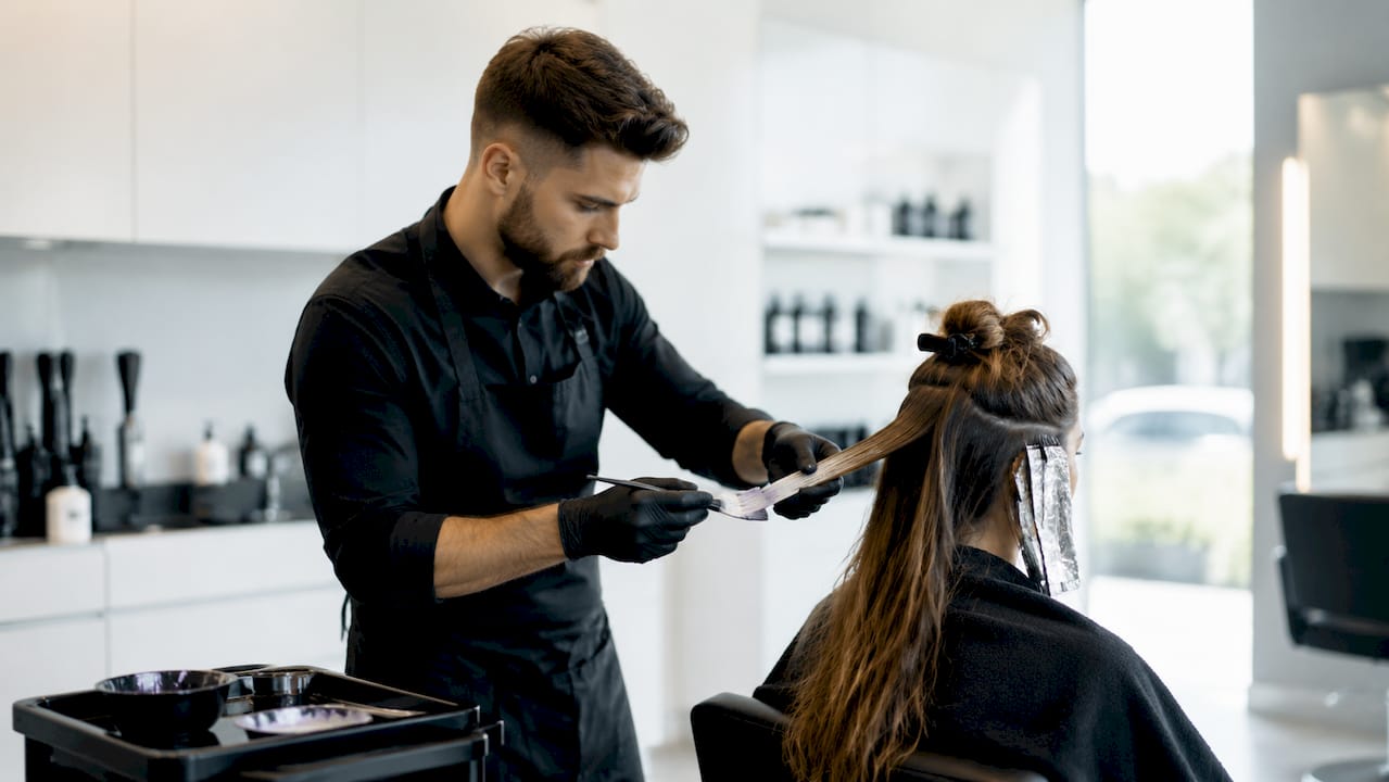 Ein Friseur trägt mit einem Pinsel Haarfarbe auf.