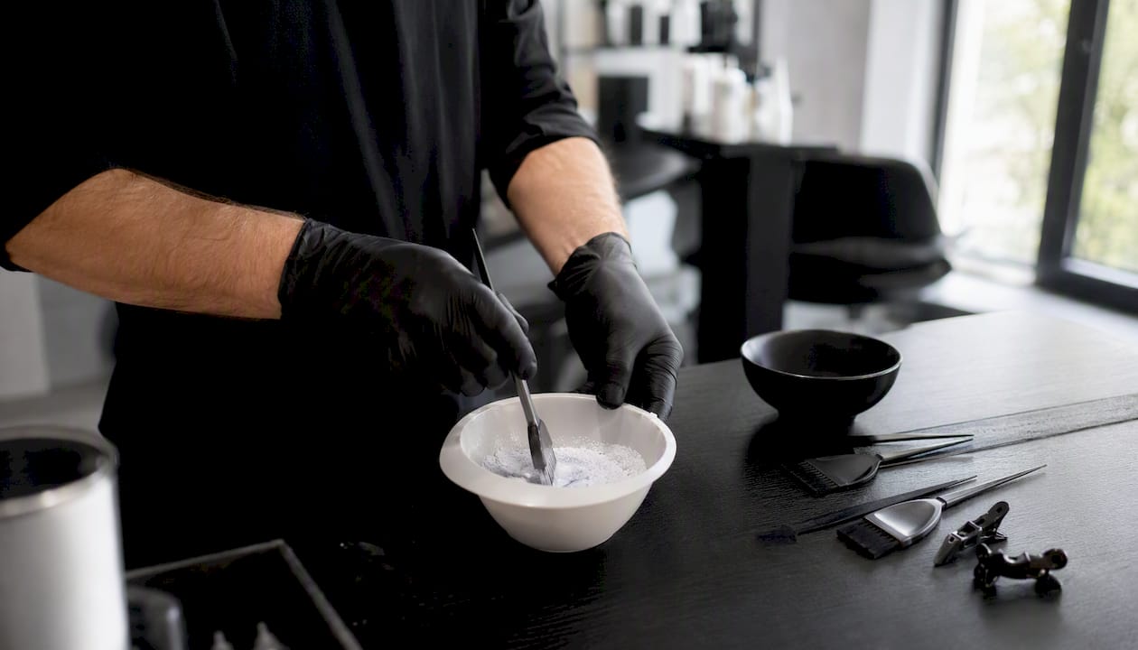 Ein Friseur rührt im Salon die Haarfarbe in einer Schale an.