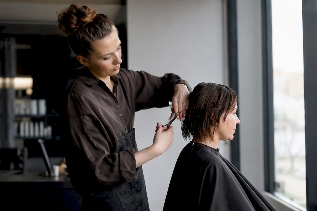 Eine Friseurin schneidet einer Frau mittleren Alters die Haare.