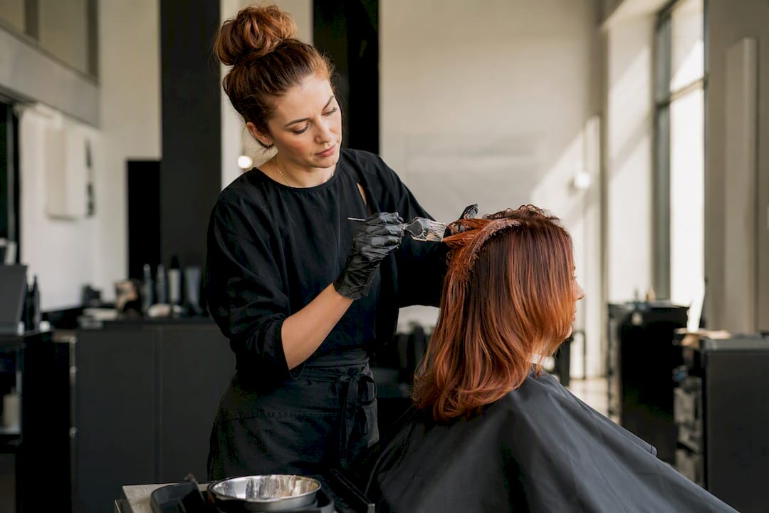Friseur trägt im Salon kupferfarbenes Haarfärbemittel auf