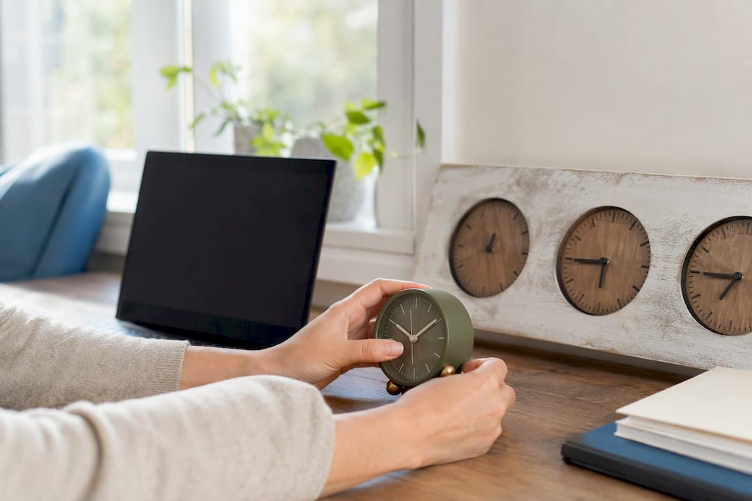 Hands adjusting desk clock near laptop