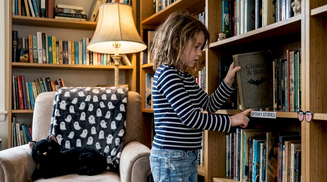 Girl reaching for spooky illustrated book on shelf