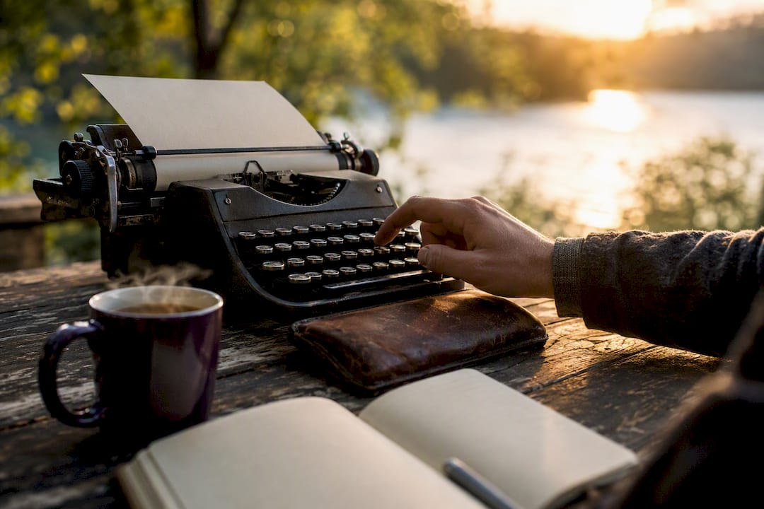 Hand typing on vintage typewriter beside coffee
