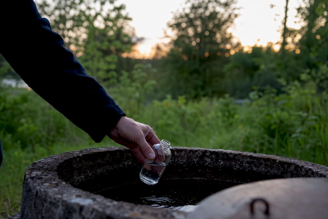 Hand som tar morgonprovs vatten från en brunn