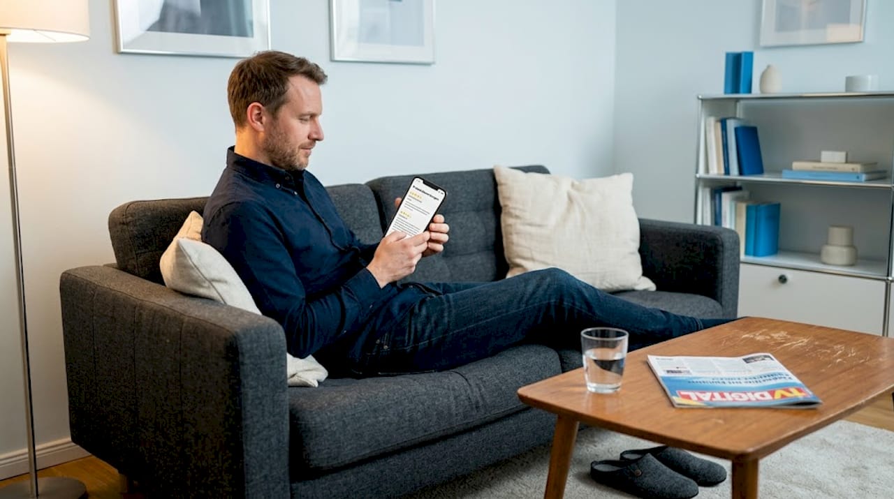 Abends sitzt ein Mann gemütlich auf dem Sofa und stöbert durch Kundenbewertungen.