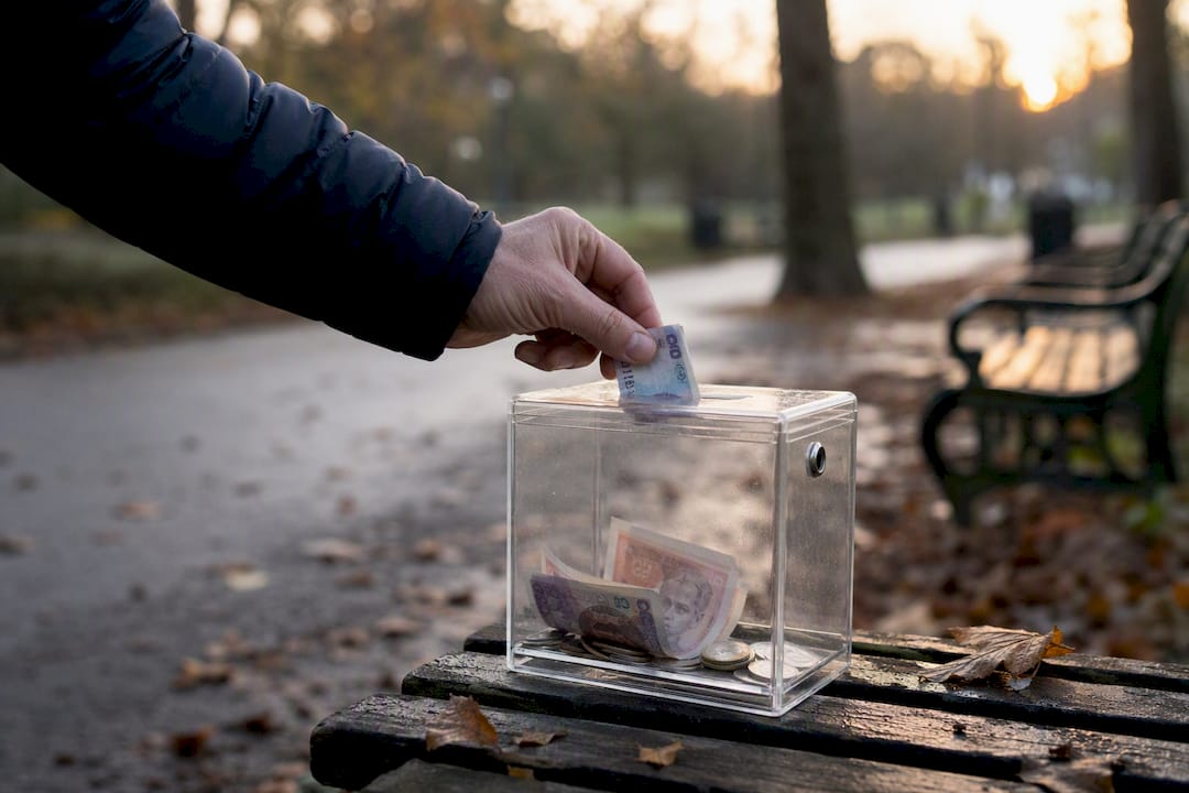 Hand inserting money in charity donation box outdoors