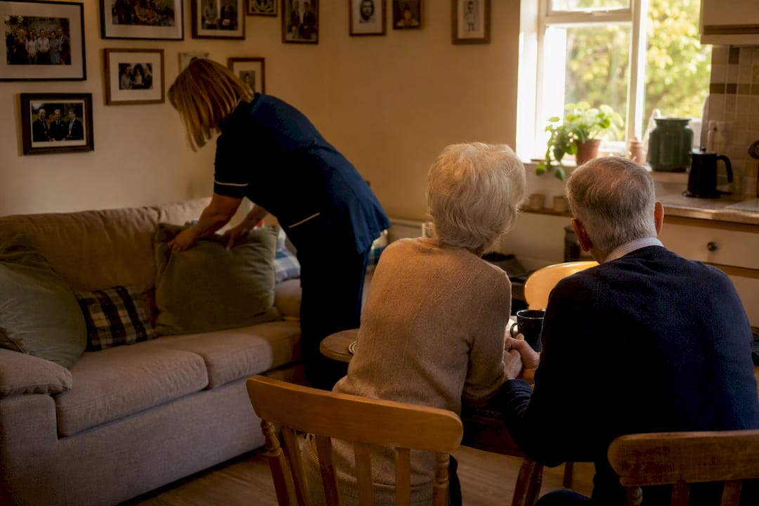 Carer adjusting cushions with elderly couple sitting together