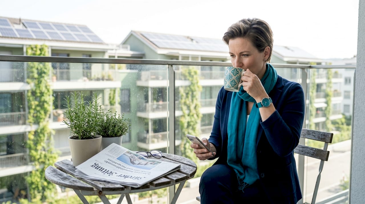 Eine Frau steht auf ihrem Balkon und blickt auf moderne, nachhaltig gebaute Wohnanlagen.