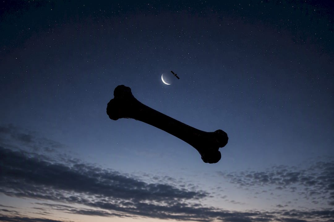 Silhouettes of spinning bone and satellite against sky
