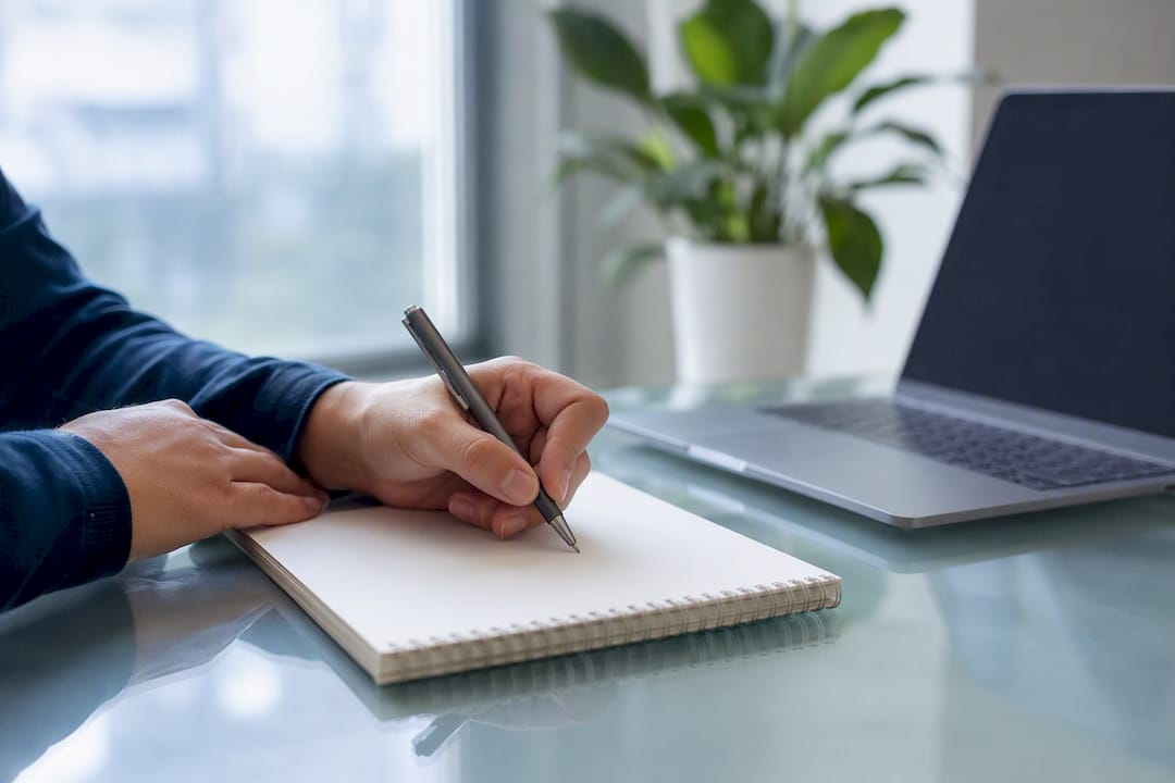 Hands writing outreach list on notepad