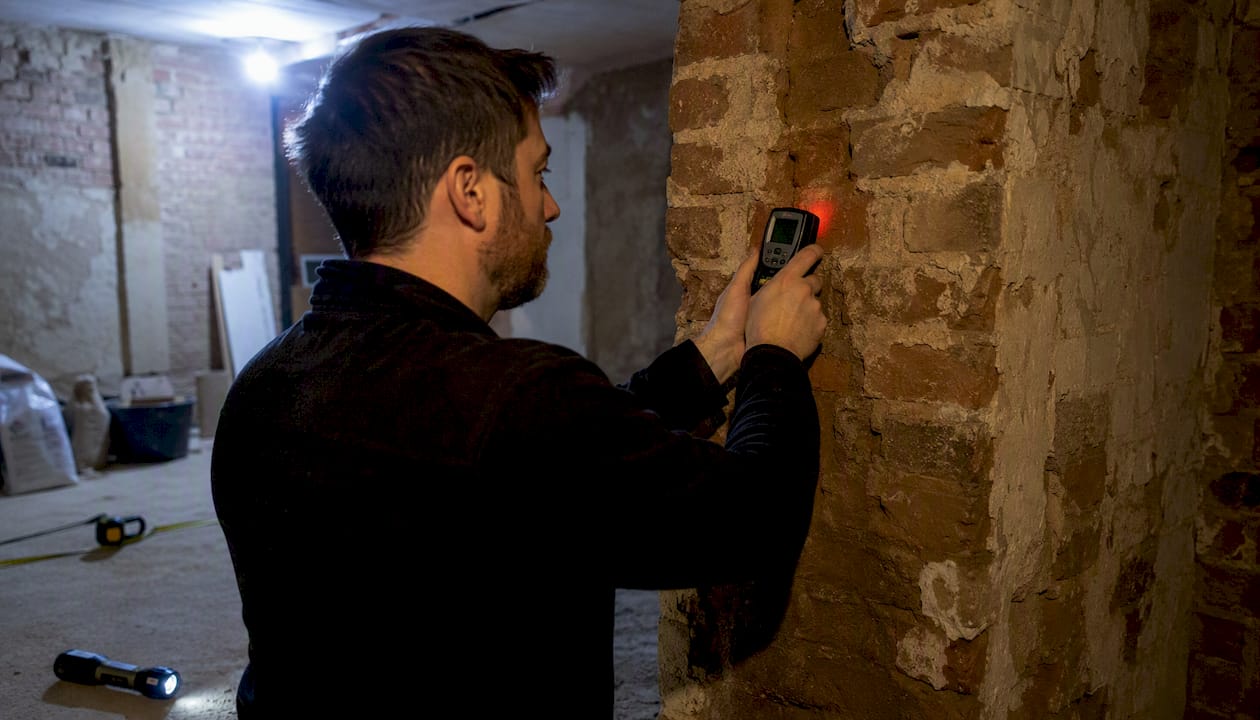 Surveyor testing brick wall moisture levels indoors