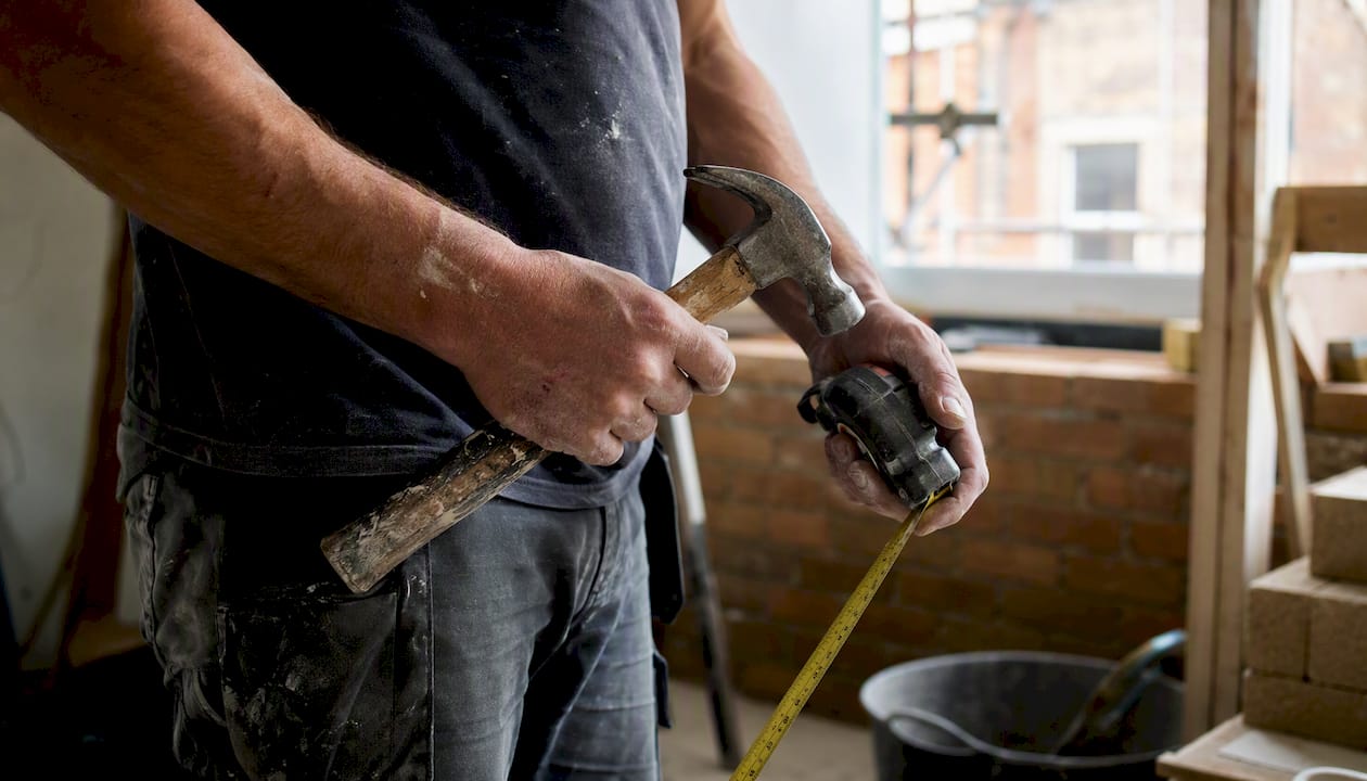 Subcontractor hands holding hammer and tape measure
