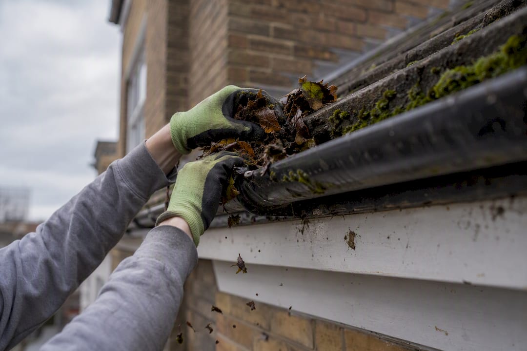 Hands cleaning gutter in spring