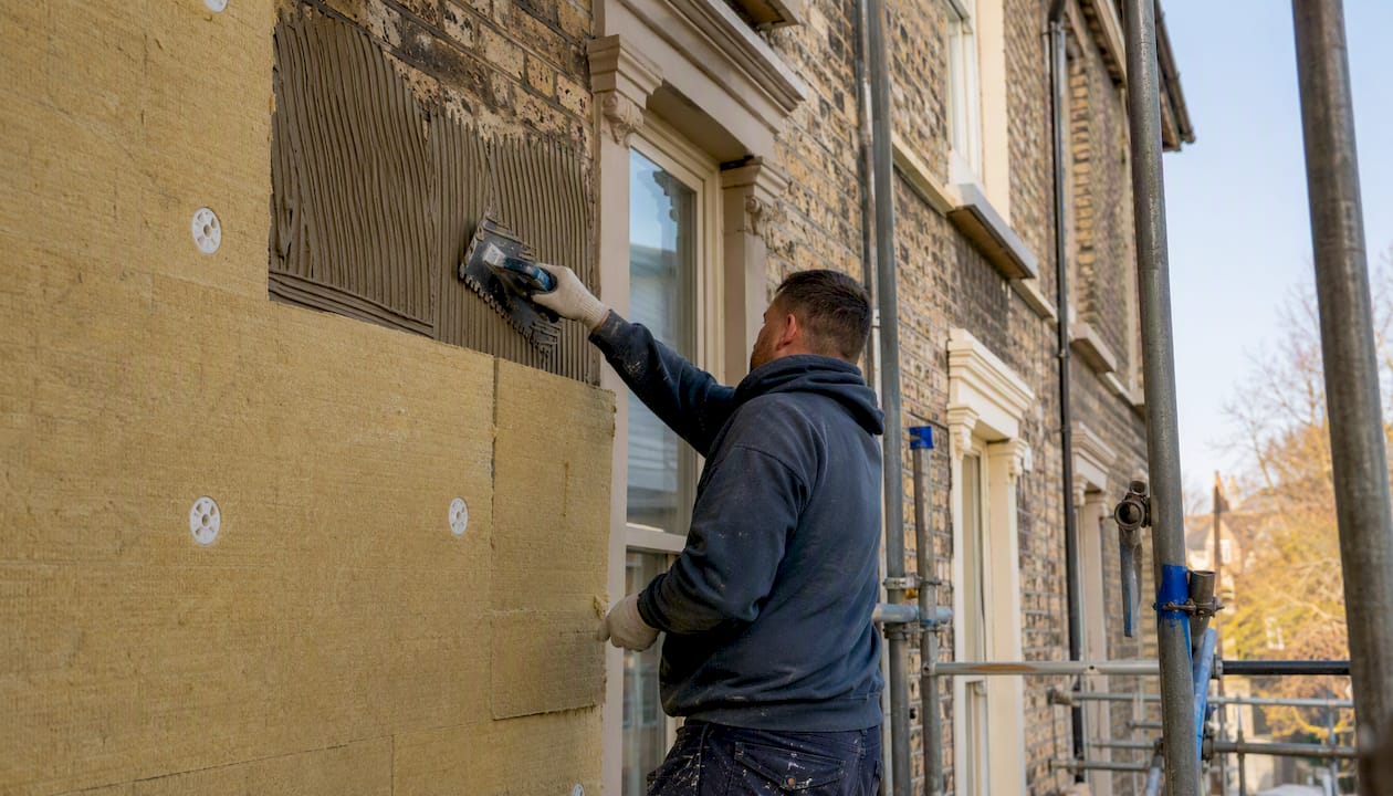 Tradesperson applying external wall insulation on brick wall
