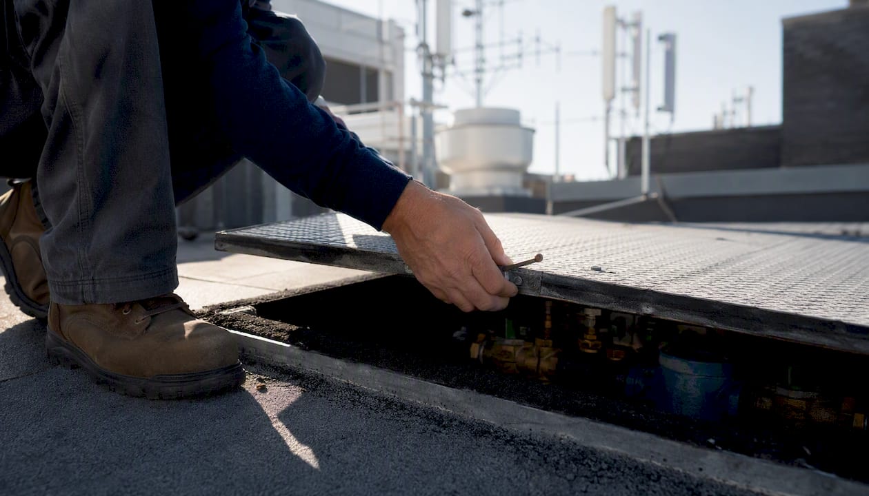 Hands opening rooftop hatch for backflow inspection