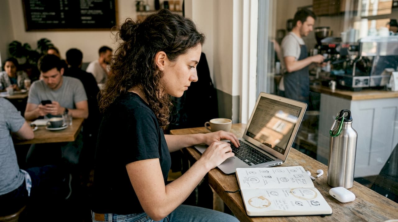 Freelancer emails clients at busy café table