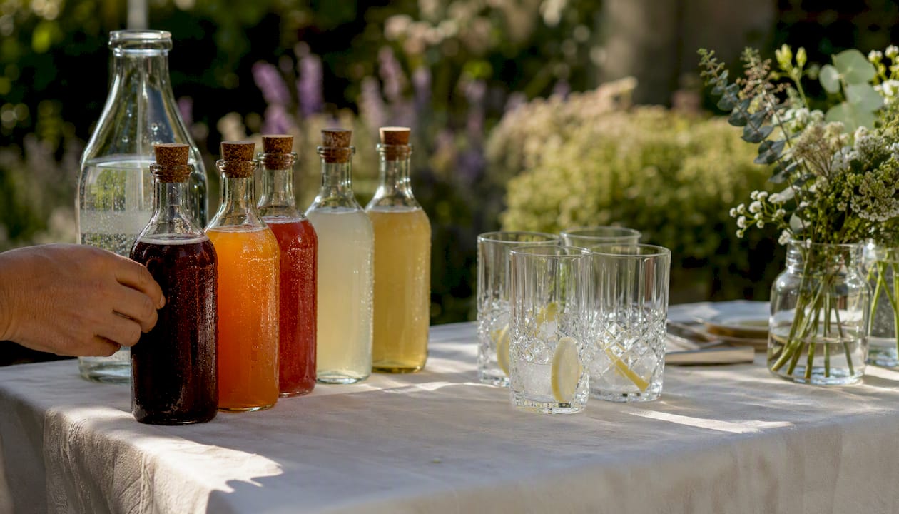 Ein liebevoll gedeckter Apéro-Tisch mit verschiedenen Sirupflaschen und sprudelndem Mineralwasser lädt zum Genießen ein.