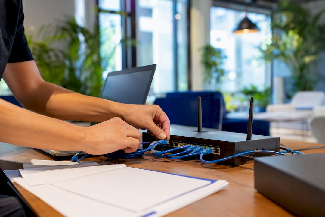 Hands connecting cables behind office desk devices