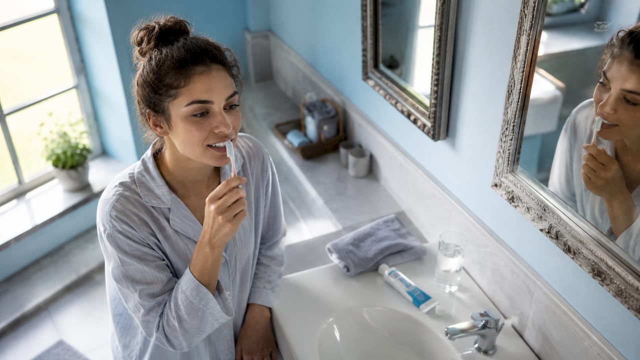 Prim-plan cu mâini care se spală pe dinți în baia de acasă