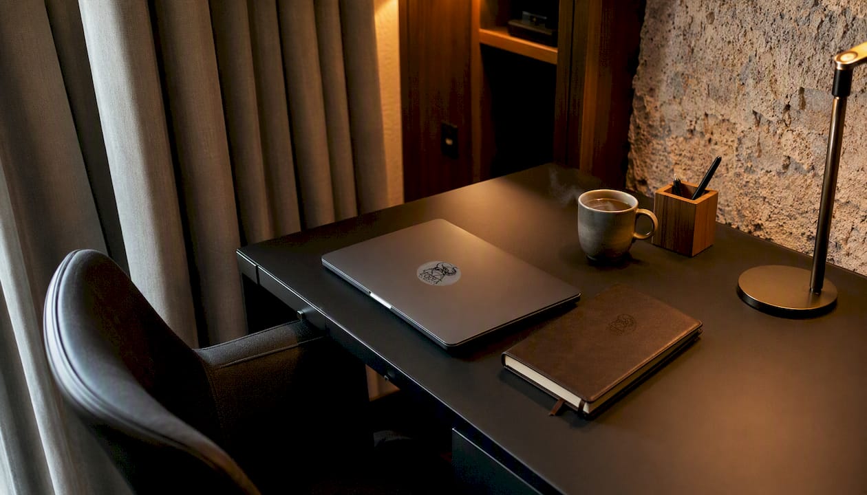 Colț de lucru amenajat în camera de hotel, cu laptopul deschis și o ceașcă de cafea alături.