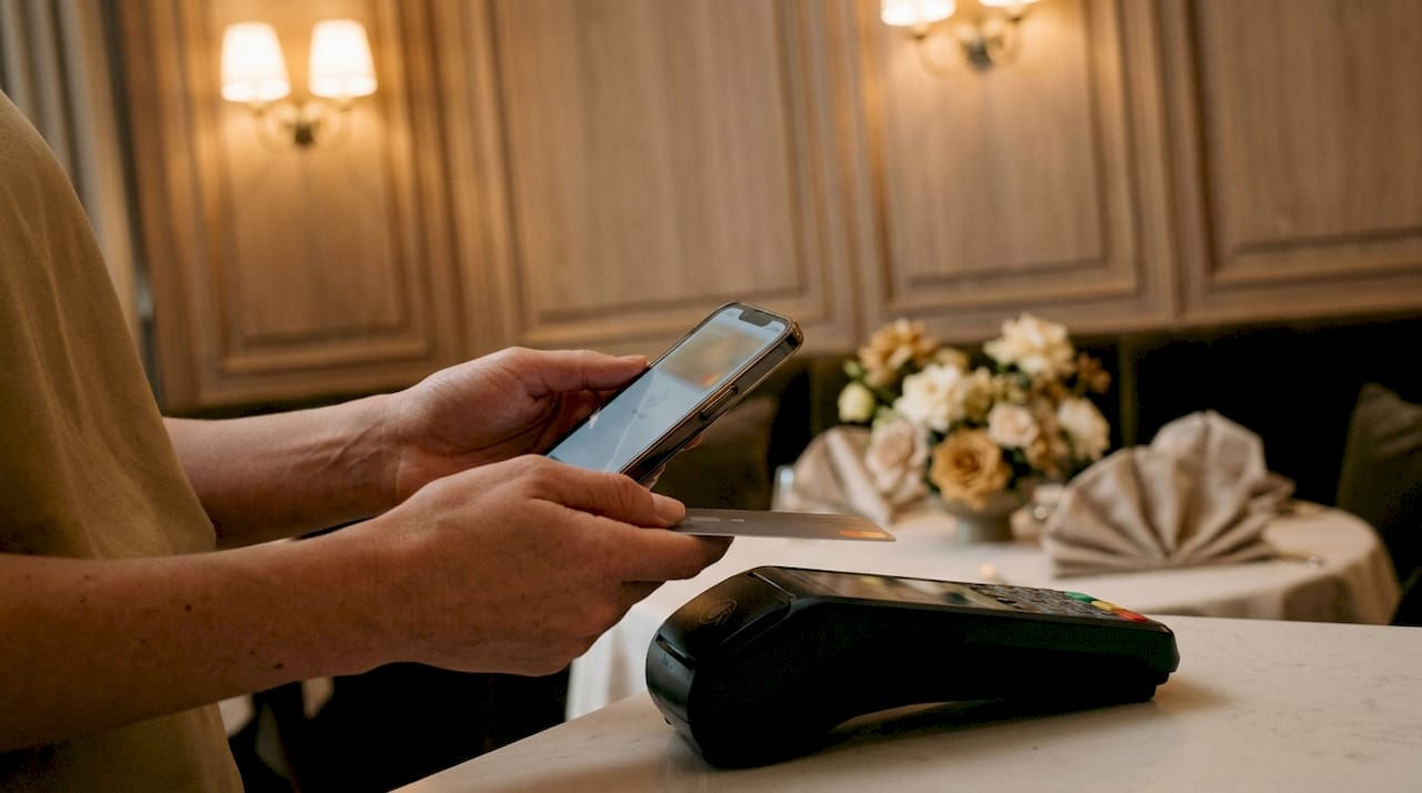 Hands using mobile phone and card to pay at terminal